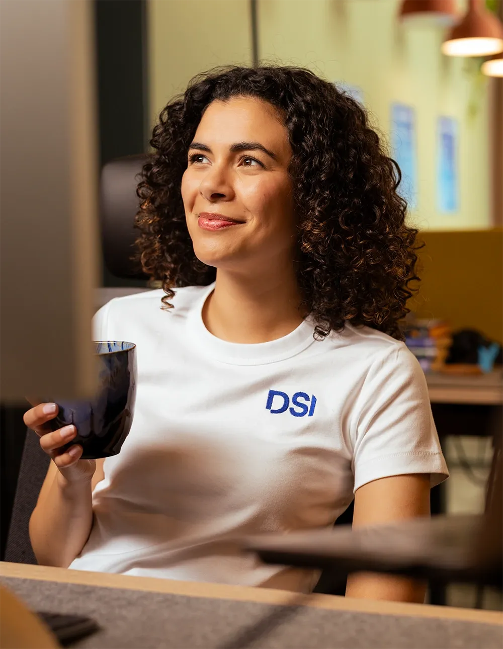 Mitarbeiterin im DSI-Shirt mit einer Tasse am Arbeitsplatz