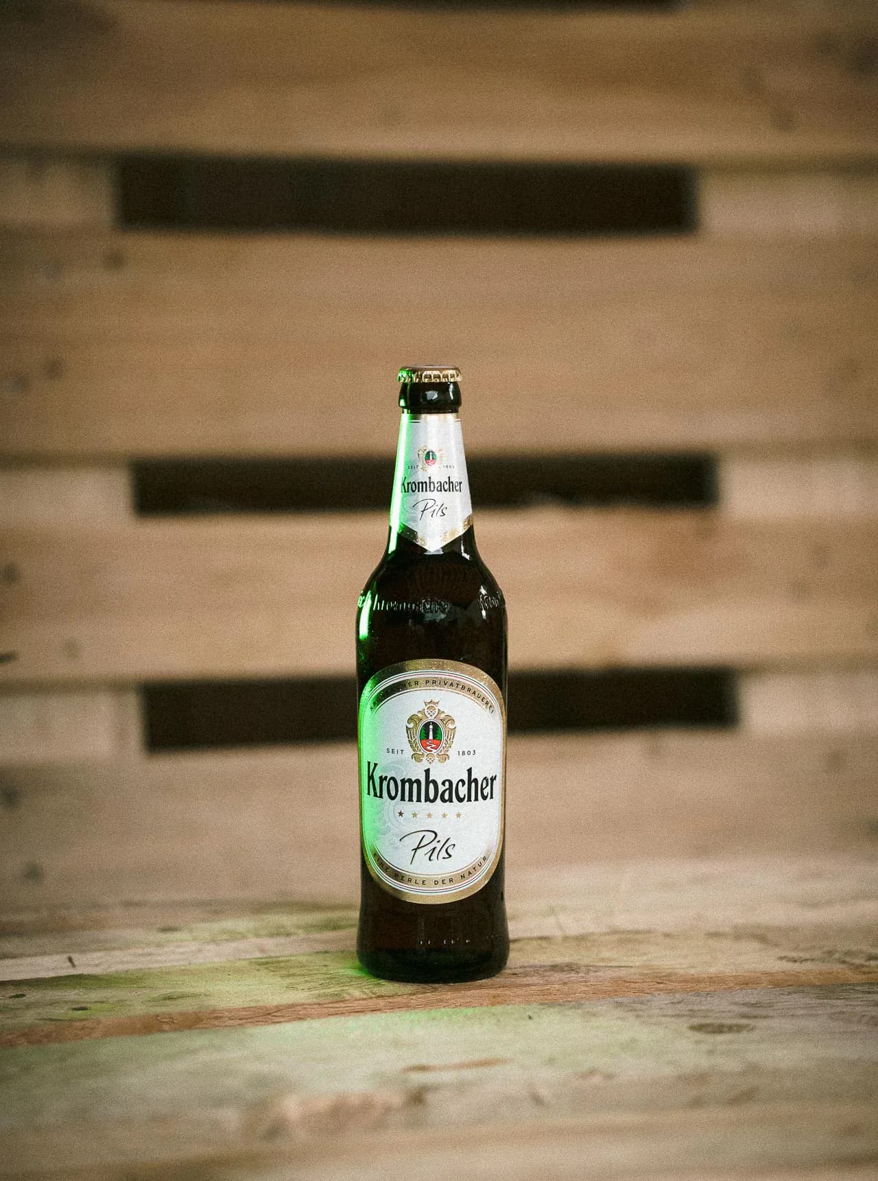 Krombacher-Bierflasche vor gestapelten Holzkisten